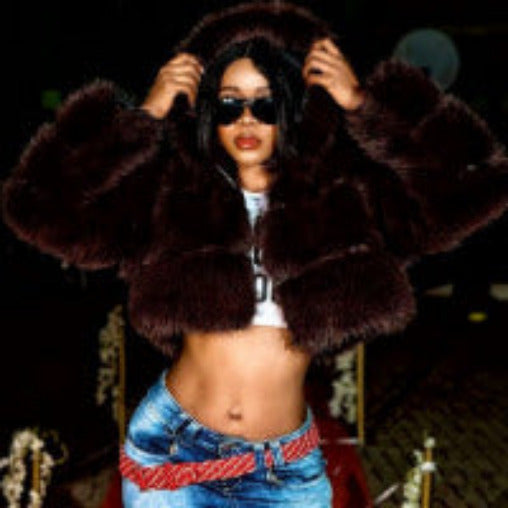 Person wearing a brown fur coat and sunglasses with a dark background